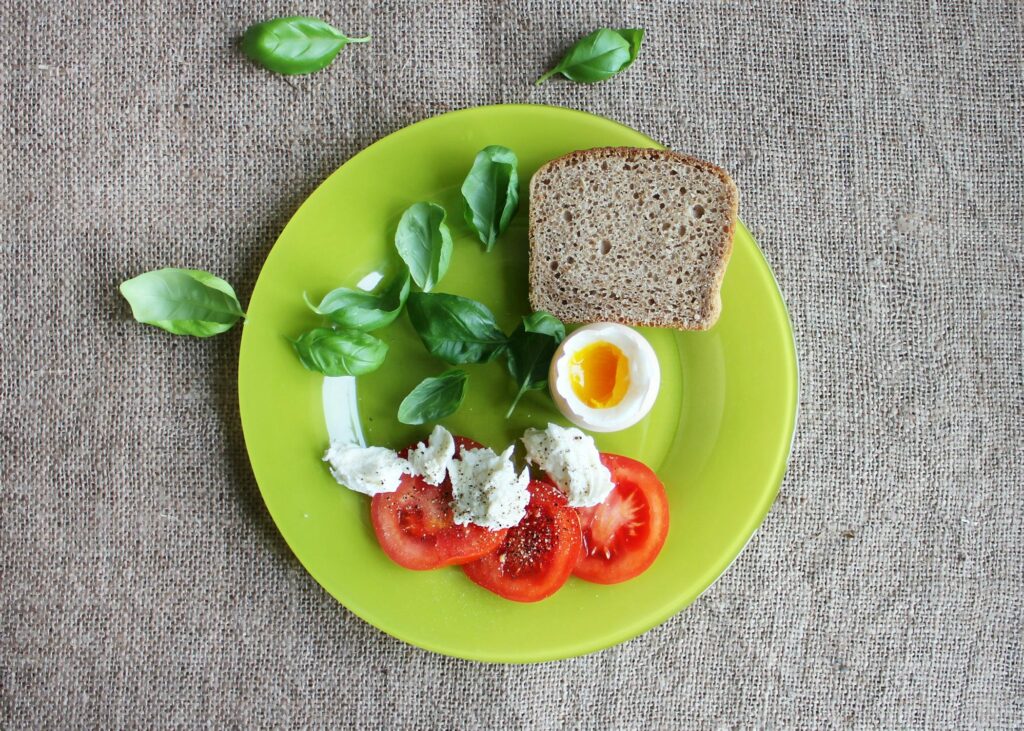 Top-down view of a breakfast plate featuring bread, soft-boiled egg, tomatoes, and basil.