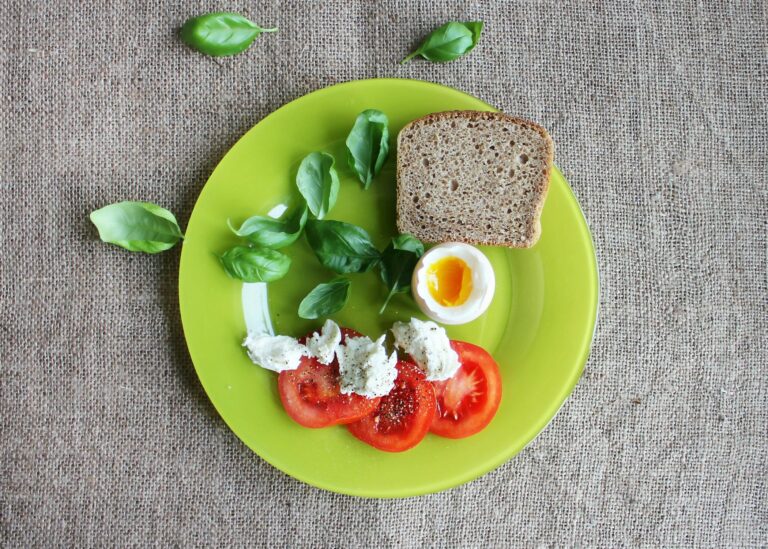 Top-down view of a breakfast plate featuring bread, soft-boiled egg, tomatoes, and basil.